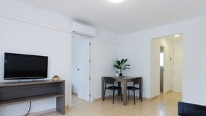 Un salon moderne avec un téléviseur à écran plat, une table à manger avec des chaises, une plante en pot et une porte blanche.