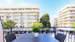 Un balcon avec une table et des chaises, donnant sur un paysage urbain composé d’immeubles à plusieurs étages et d’un ciel dégagé.