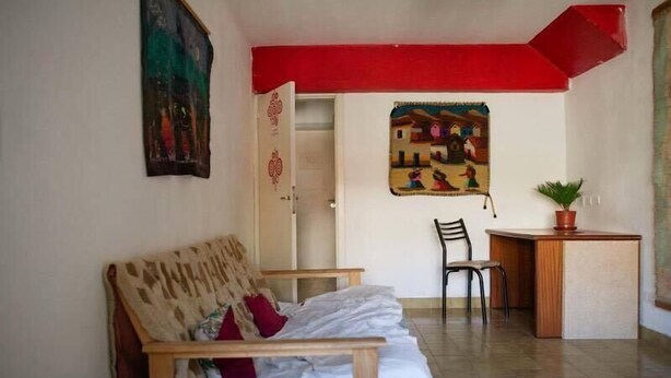 A room with a sofa, a small table, a chair, and a painting on the wall. - Phoenix Hostel (San Carlos de Bariloche)