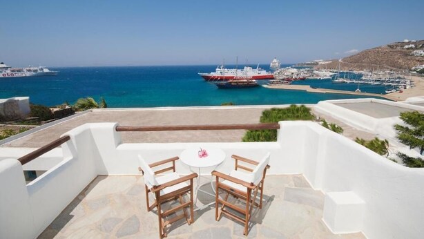 A terrace with two wooden chairs and a small table, overlooking a marina with boats and a beach. - MEGAS ROOMS (Tourlos)