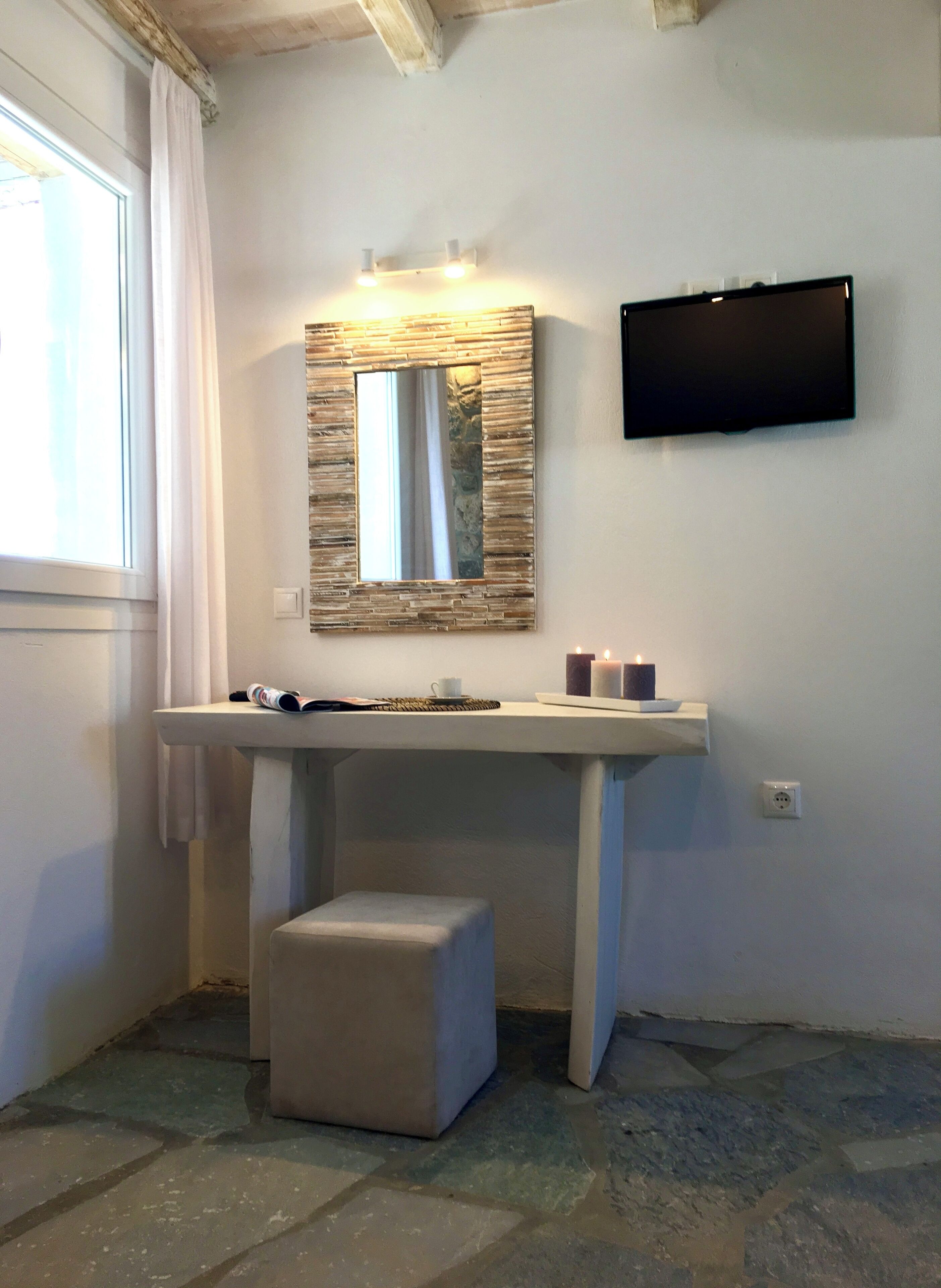 A bathroom with a vanity, a mirror, a television mounted on the wall, and a window with curtains.