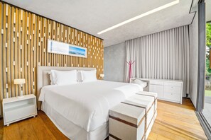 A modern hotel room with a large bed, wooden panel wall, white furniture, and a view of greenery. - Solar La Luna (Sao Pedro)