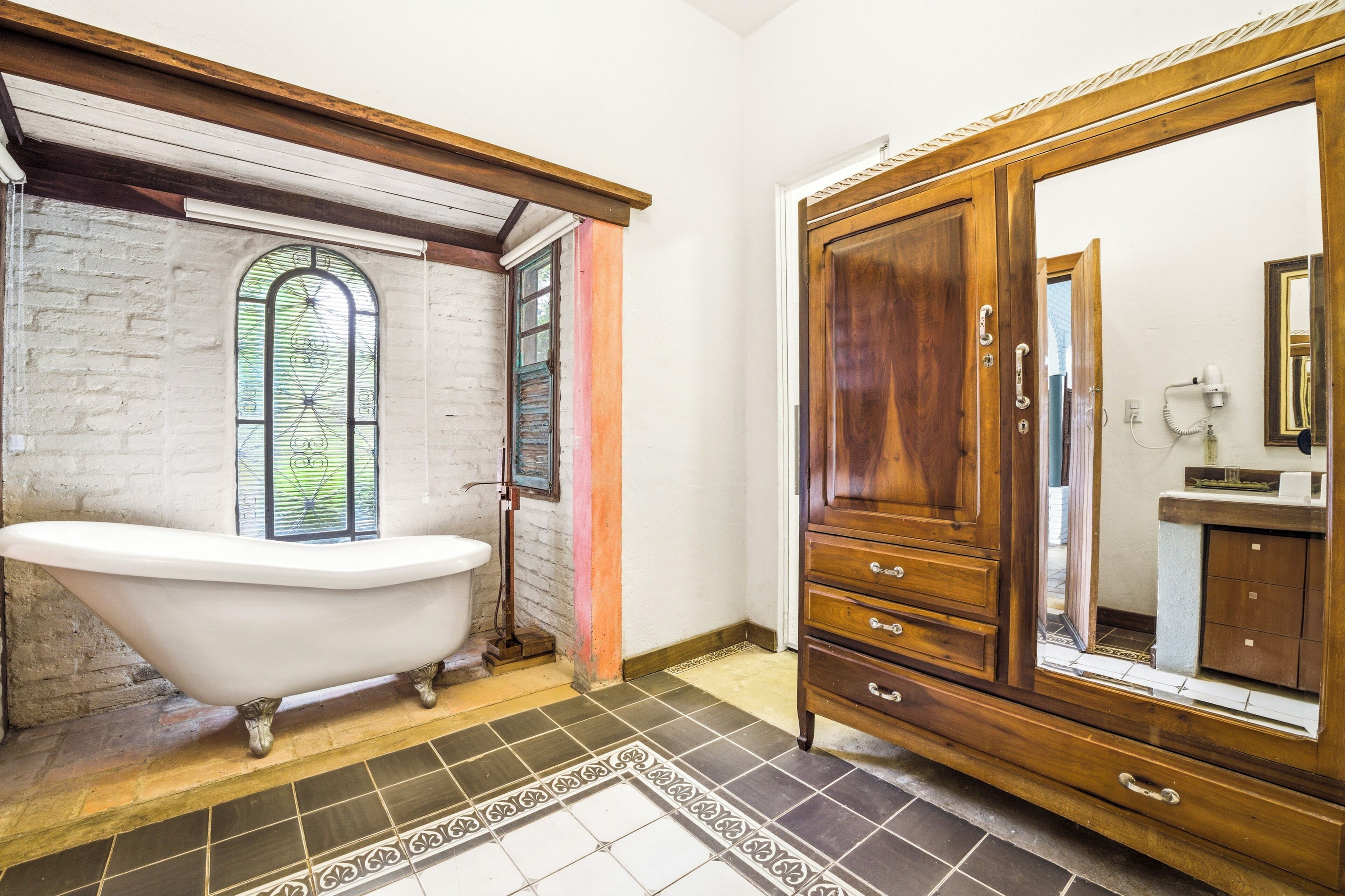Un baño con una bañera de patas de león, un tocador de madera, un espejo y un ventanal con un diseño de vitral.