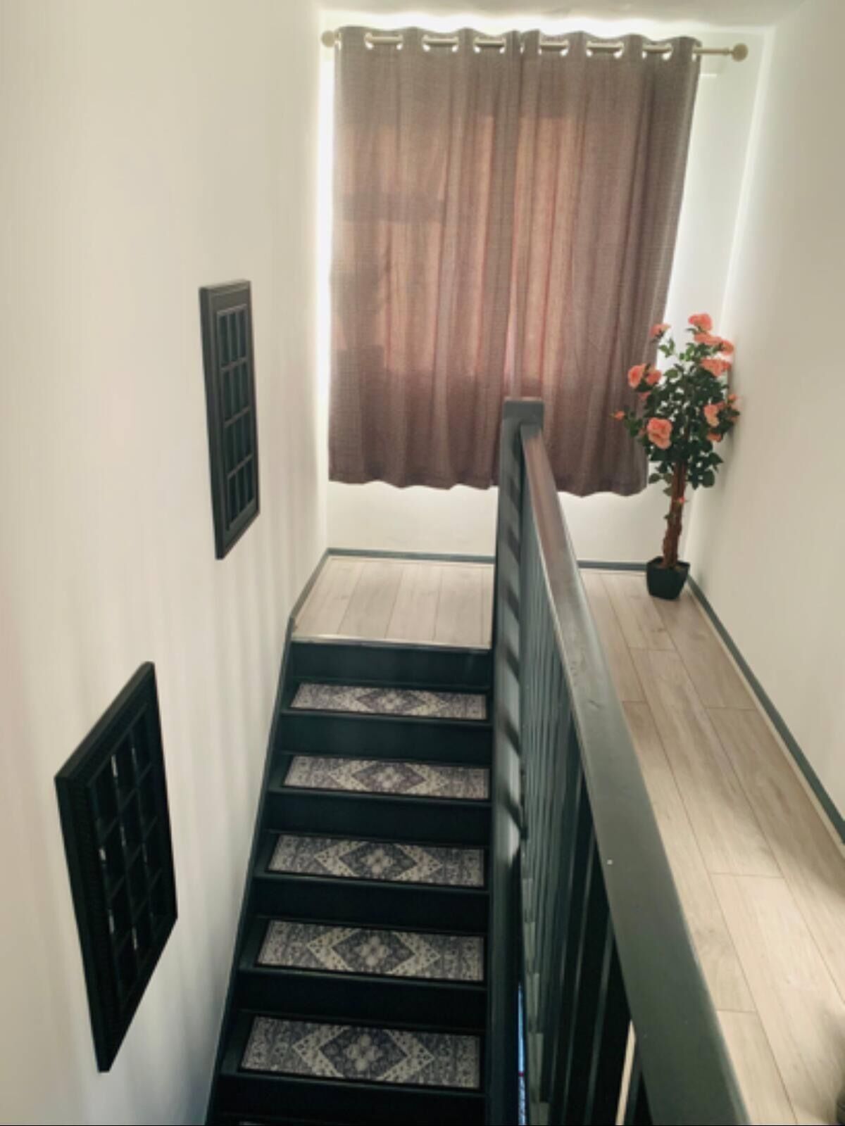 A staircase with a black railing, patterned carpet, and a brown curtain at the top.