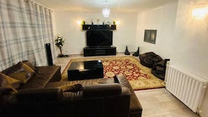 A living room with a brown leather sofa, a black entertainment unit, a patterned rug, and a white radiator. - Surrey Hills Retreat - 2 Bed - Easy Access to Central London (Ash)