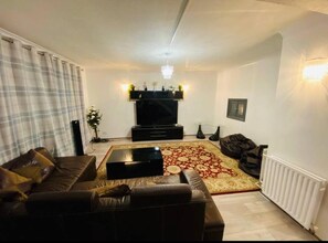 A living room with a brown leather sofa, a black entertainment unit, a patterned rug, and a white radiator. - Surrey Hills Retreat - 2 Bed - Easy Access to Central London (Ash)