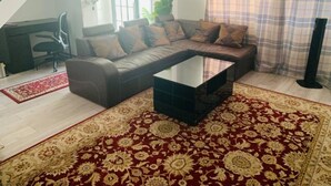 A living room with a sectional sofa, a glass coffee table, and a red patterned rug. - Surrey Hills Retreat - 2 Bed - Easy Access to Central London (Ash)