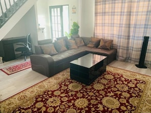A living room with a sectional sofa, a glass coffee table, and a red patterned rug. - Surrey Hills Retreat - 2 Bed - Easy Access to Central London (Ash)