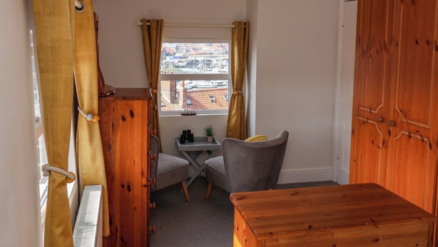 A small, cozy room with a wooden wardrobe, a desk with a chair, and a view of the city through a window. - Harbour View (Whitby)