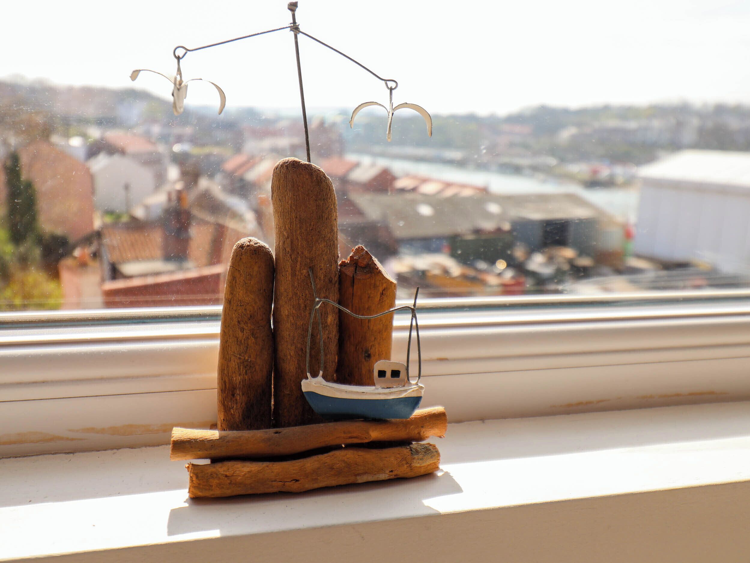 A model boat on a wooden base by a window overlooking a town.