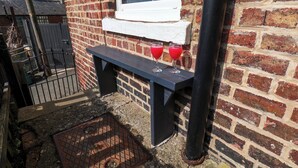 A brick building with a window, a bench, and two glasses of red drink on the bench. - Harbour View (Whitby)