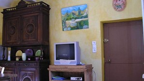 A room with a wooden cabinet, a television on a wooden stand, a painting on the wall, and a door. - Gites in Cévennes bed linen/towel rental possible No pets allowed (le martinet)