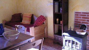 A cozy room with a wooden sofa, a dining table with a clear bowl, a bookshelf, and a vintage stove. - Gites in Cévennes bed linen/towel rental possible No pets allowed (le martinet)