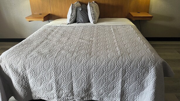A neatly made bed with a patterned bedspread, two pillows, and two bedside lamps on wooden nightstands.