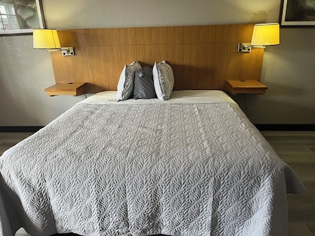 A neatly made bed with a patterned bedspread, two pillows, and two bedside lamps on wooden nightstands.
