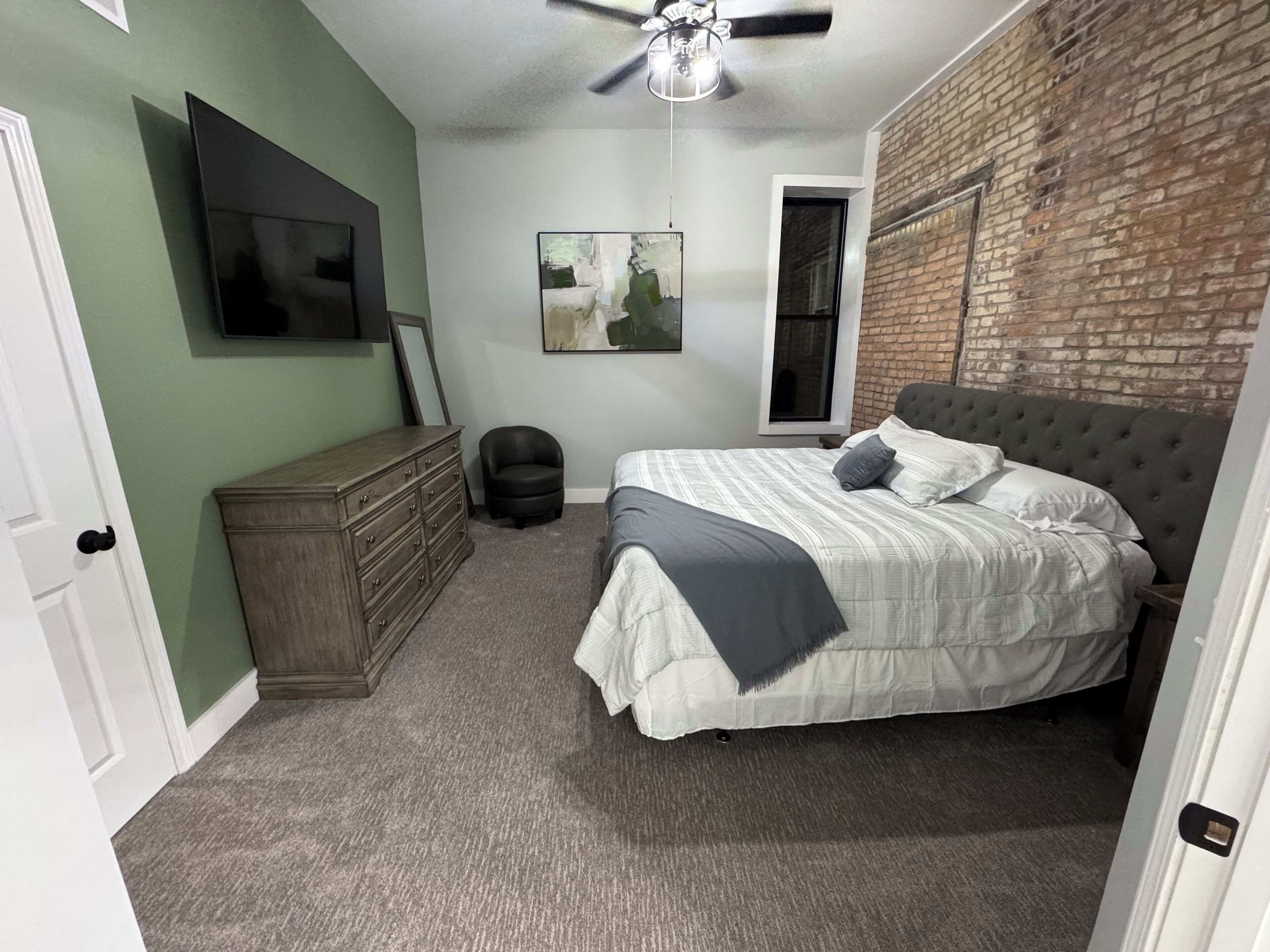 Un dormitorio con cama, cómoda y pared de ladrillo.
