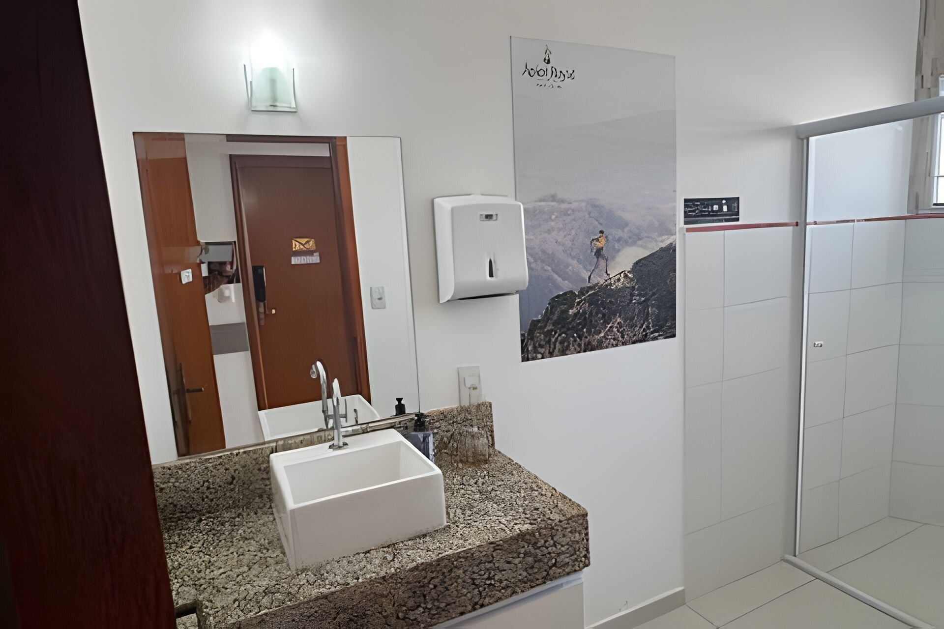 A bathroom with a granite countertop sink, a hand dryer, a poster of a mountain climber, and a shower area.
