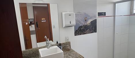 A bathroom with a granite countertop sink, a hand dryer, a poster of a mountain climber, and a shower area.