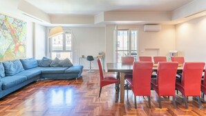 A modern living room with a blue sectional sofa, a dining table with red chairs, and a herringbone wood floor. - VATICAN PIXEL APARTMENTS®️ (Roma)