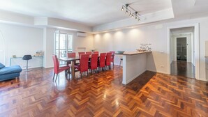 A spacious living area with a wooden herringbone floor, a dining table with red chairs, a blue sofa, and a modern pendant light fixture. - VATICAN PIXEL APARTMENTS®️ (Roma)