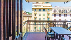 A balcony with a table and chairs, overlooking a row of multi-story buildings. - VATICAN PIXEL APARTMENTS®️ (Roma)