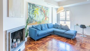A modern living room with a blue sectional sofa, a fireplace, a large abstract painting, and a floor lamp. - VATICAN PIXEL APARTMENTS®️ (Roma)