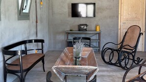 A dining area with a wooden table, two black chairs, a wicker chair, a television mounted on the wall, and a door. - Papalei La Maison (Sicilia)