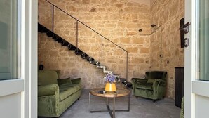 A cozy living room with a stone wall, a staircase, and two green armchairs. - Papalei La Maison (Sicilia)
