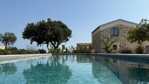 A clear swimming pool with a stone building in the background. - Papalei La Maison (Sicilia)