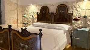 A bedroom with a wooden bed, a nightstand, and a stone wall. - Papalei La Maison (Sicilia)
