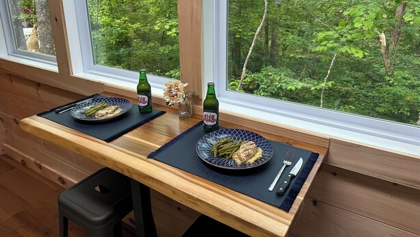 A dining table with two plates of food, two beer bottles, and a vase with flowers.