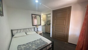Ein Schlafzimmer mit Bett, Nachttisch, Spiegel und einer Tür, die in eine Küche führt.