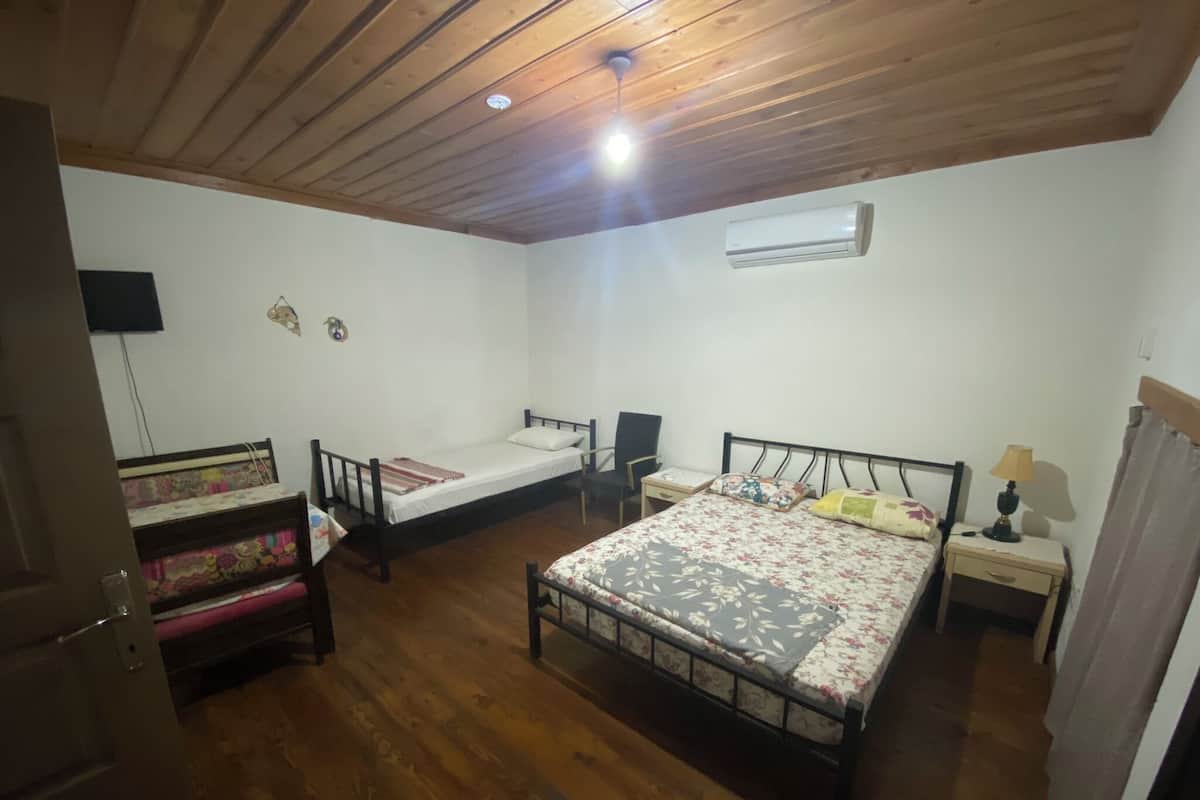 A room with two beds, a desk, a chair, an air conditioning unit, and a television on the wall.