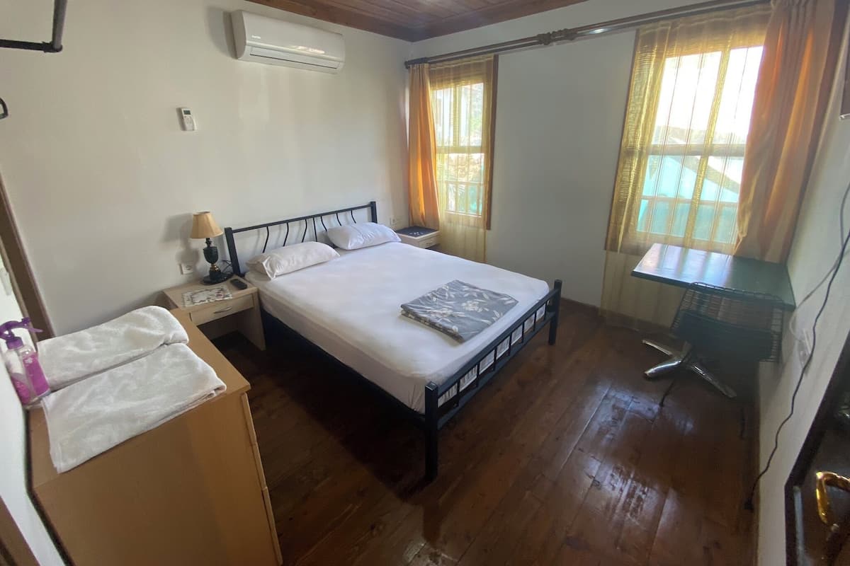 A bedroom with a bed, bedside tables, an air conditioner, a desk, and a chair.