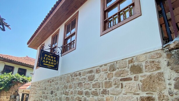 Ein zweistöckiges Gebäude mit einer Stein-Fassade und Holzfensterrahmen. Ein Schild weist auf einen Hafen und einen Ort namens Limon Apart hin.