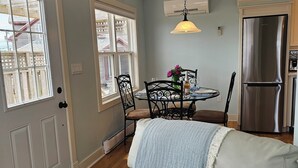 A cozy living room with a light-colored sofa, a dining table with chairs, and a kitchen area with a refrigerator. - Cozy Cottage 50 meters from the Ocean (North Rustico)