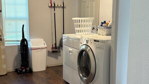 Un lavadero equipado con lavadora y secadora de carga frontal, un aspirador, una mopa y una cesta para la ropa.