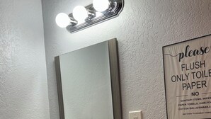 Un baño con lavamanos, espejo y un letrero que indica tirar únicamente papel higiénico.