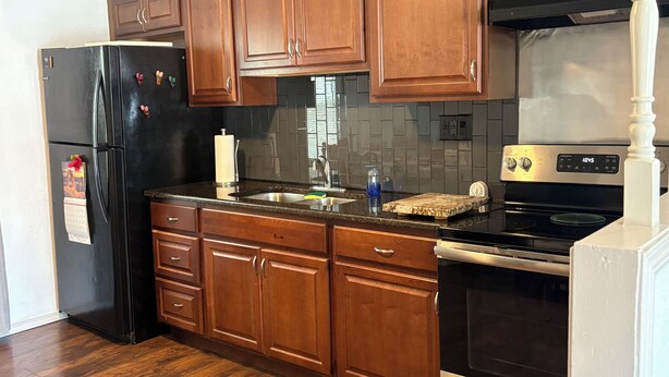 Una cocina con armarios de madera, un refrigerador negro, una estufa de acero inoxidable y salpicadero de azulejos.