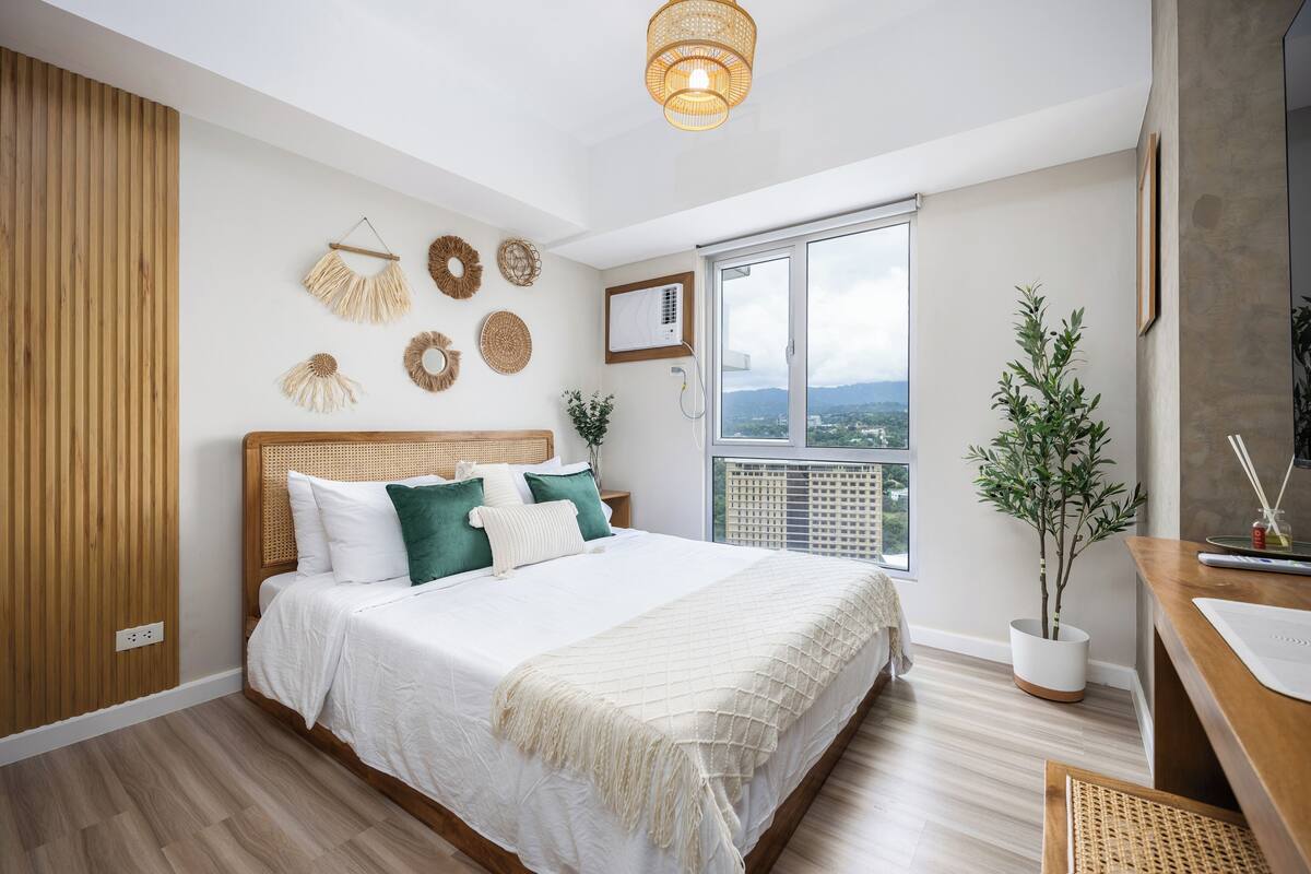 Un dormitorio con una cama grande, una planta en maceta, un ventanal con vistas y una lámpara en el techo.