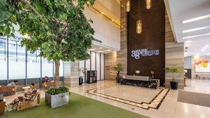 A modern hotel lobby with a reception desk, seating area, and a large tree. - Avida Riala IT Park - Virgo Nest Rentals (Cebu)