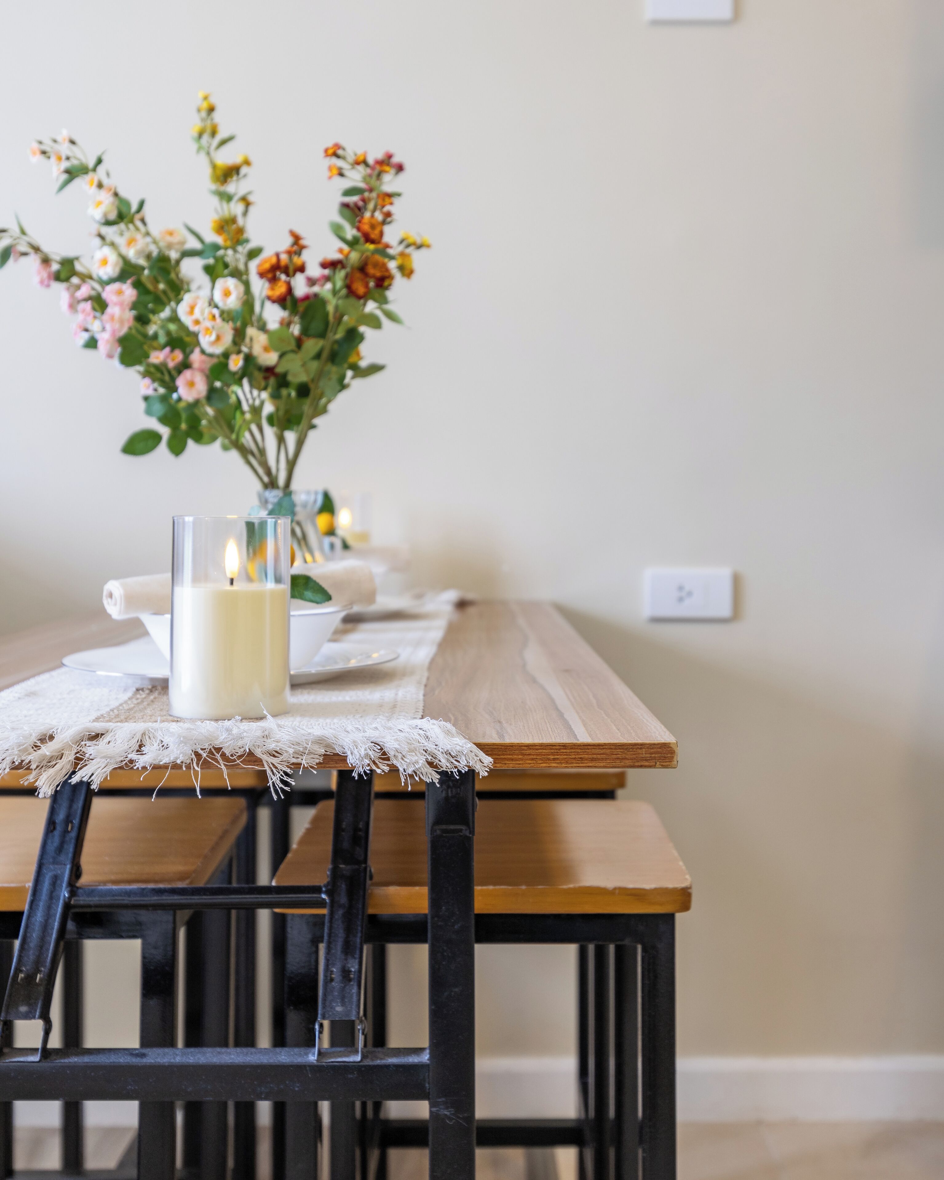 A dining table with a candle and flowers, a chair, and a wall socket.