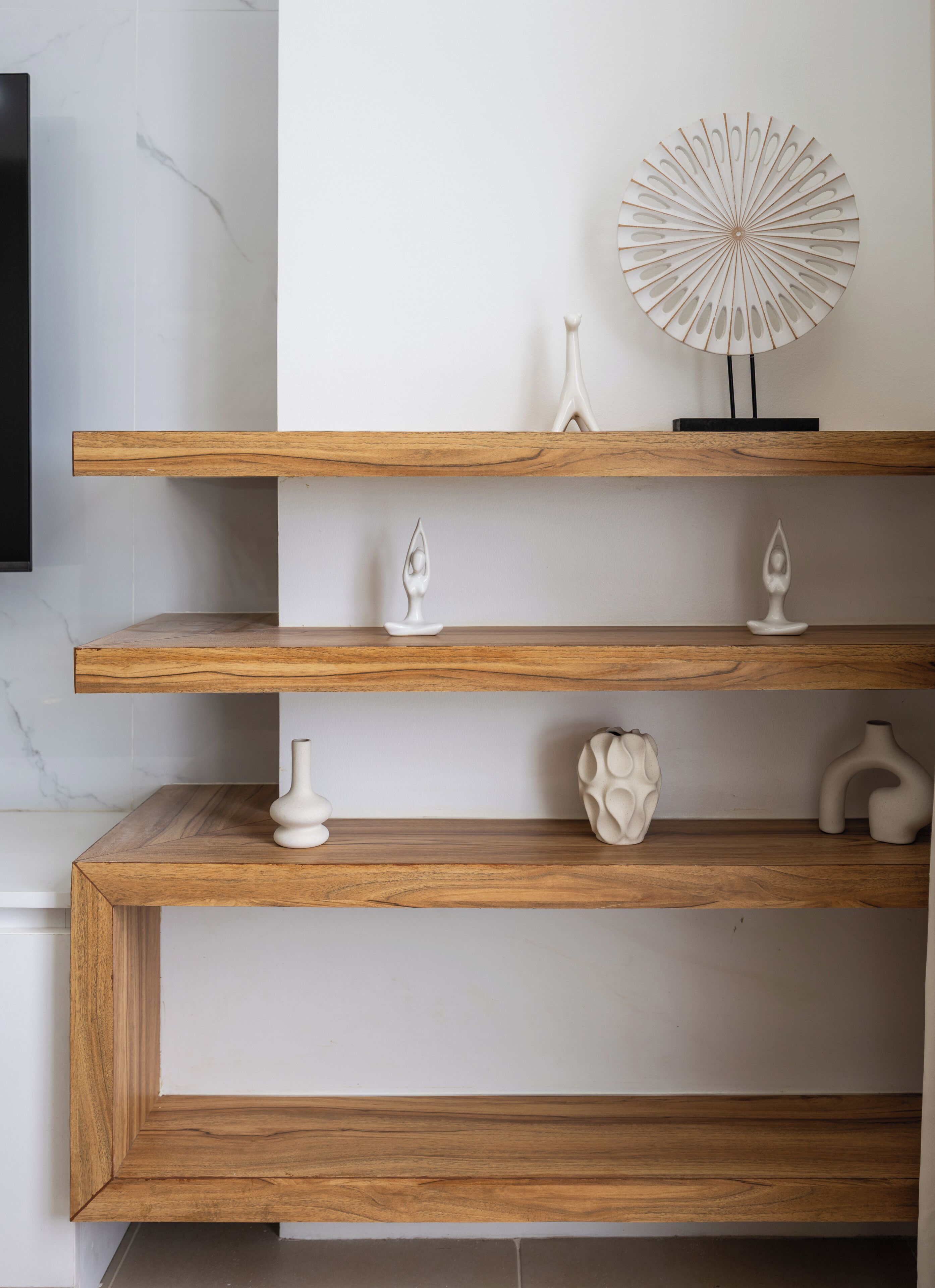A modern interior with three wooden shelves displaying various white decorative items.