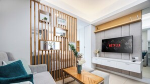 Een moderne woonkamer met een bank, een salontafel, een aan de muur bevestigde televisie en een houten scheidingswand met planken.
