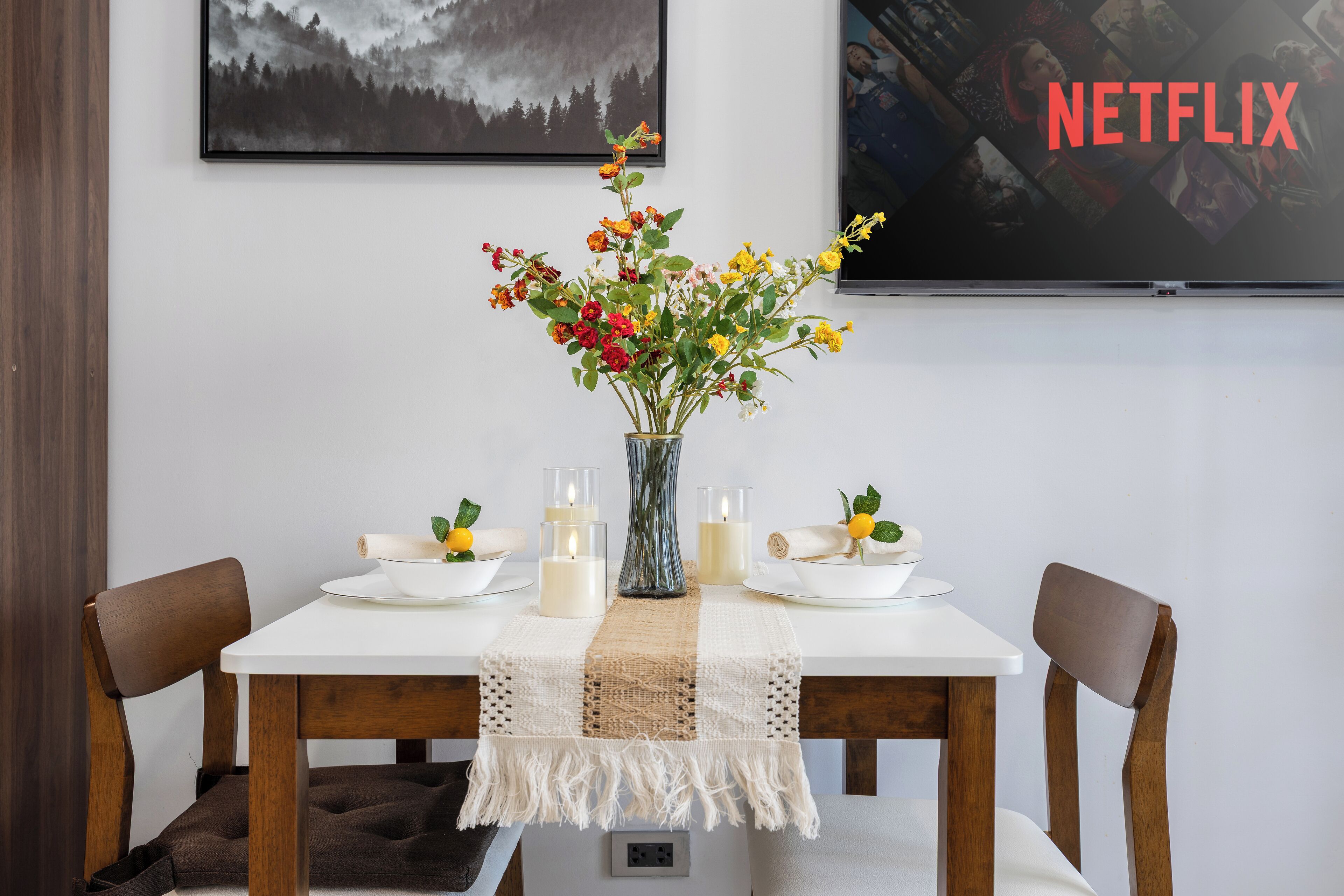A dining table with a vase of flowers, candles, and a placemat.