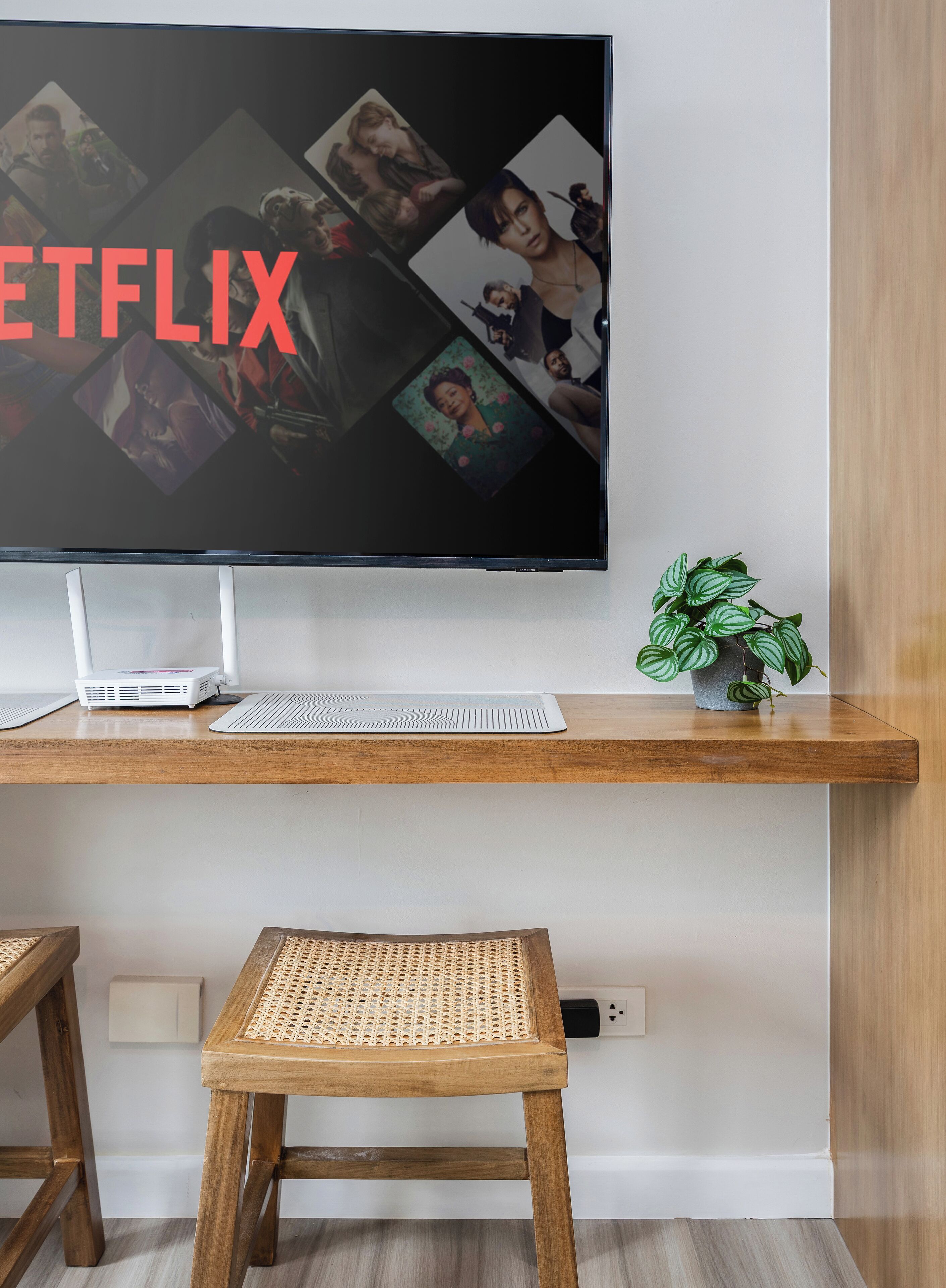 Una sala moderna con un televisor de pantalla plana grande montado en una pared de madera, una computadora de escritorio, un teclado, una pequeña planta en maceta y una silla tejida.
