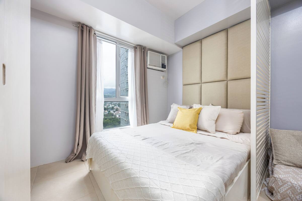 Un dormitorio con una cama grande, una ventana con cortinas y vistas a la ciudad.