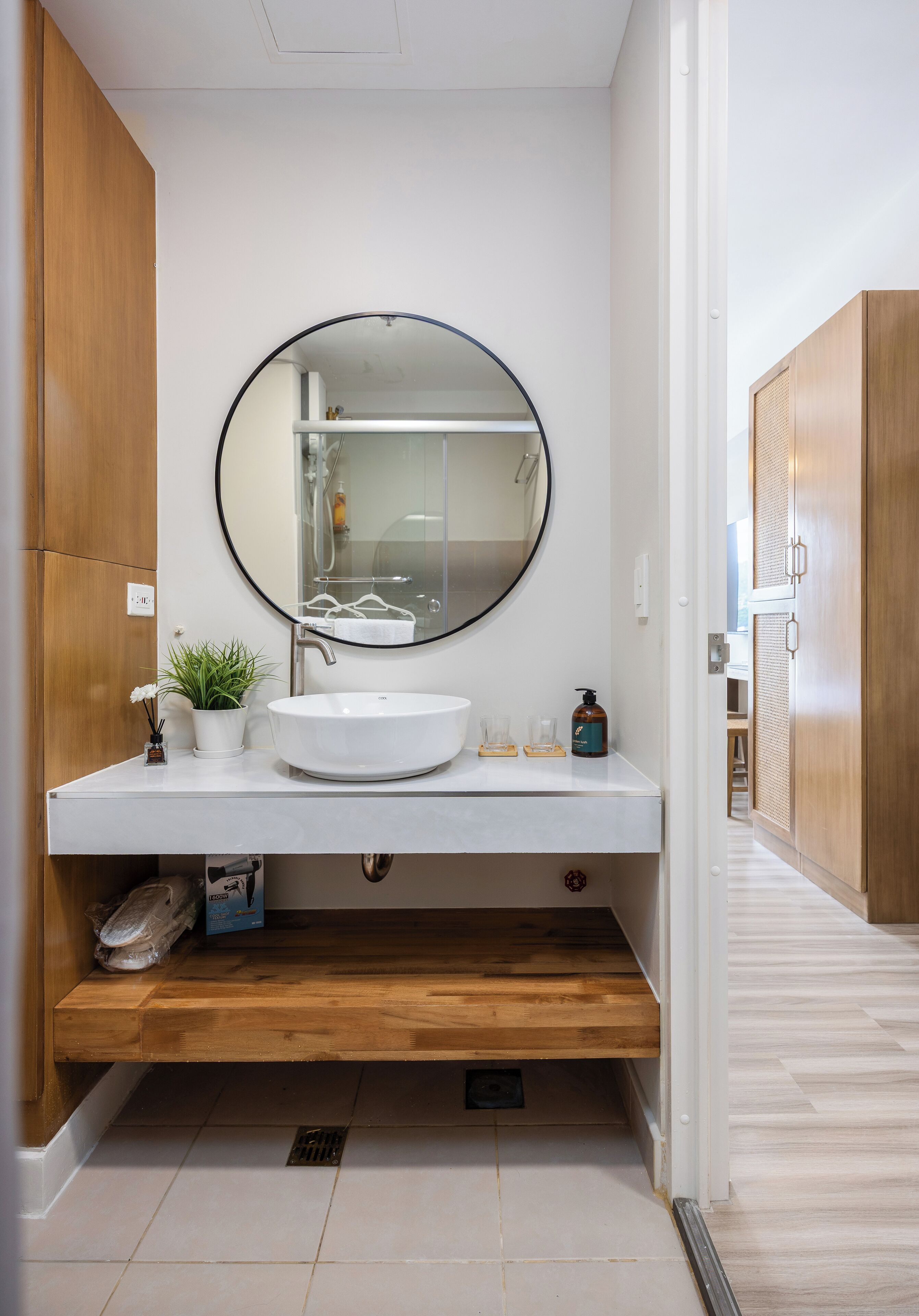 Un baño moderno con un lavabo blanco, un espejo redondo y muebles de madera.