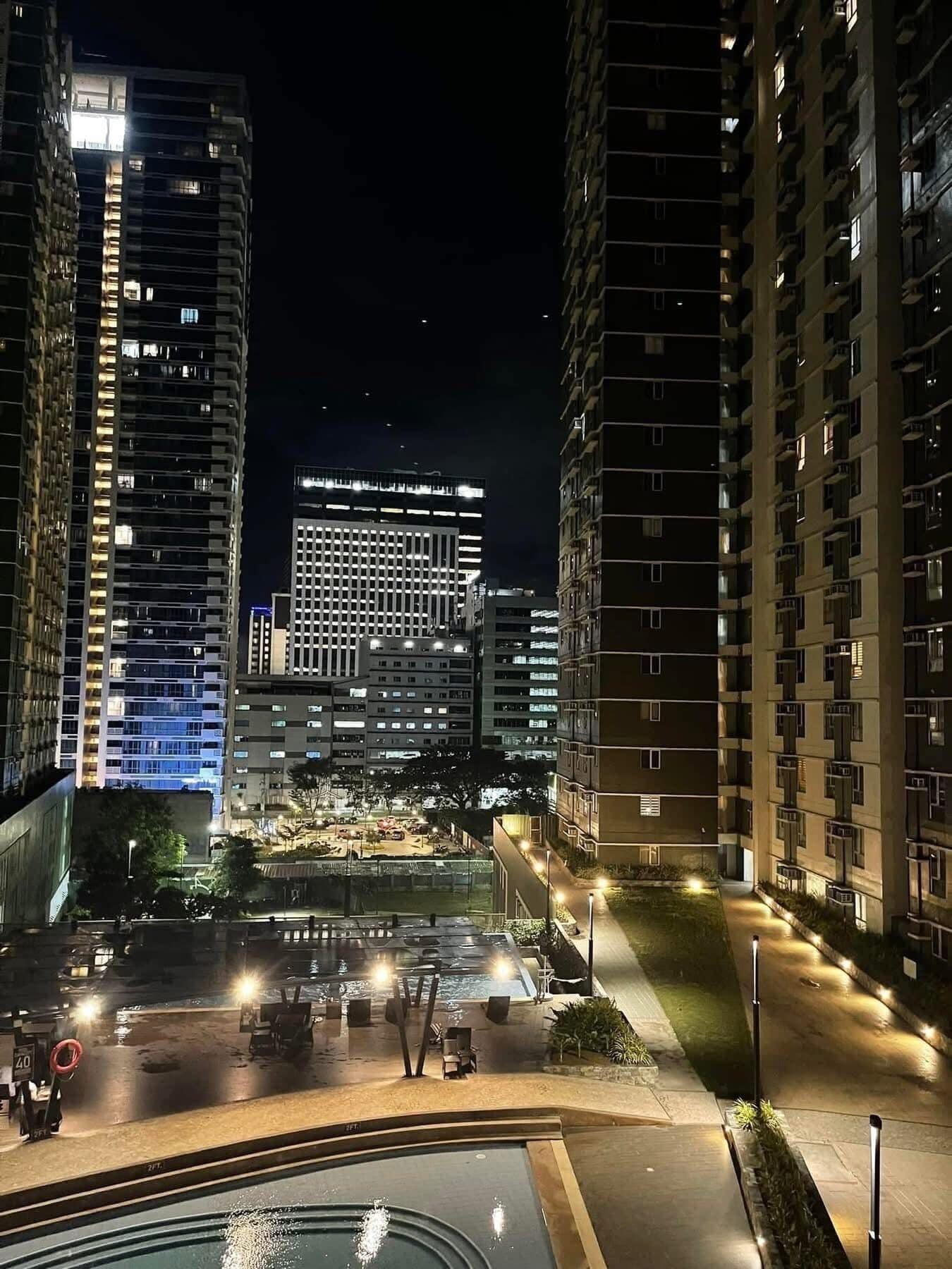 A nighttime view of a high-rise residential building with multiple floors, a central courtyard with a swimming pool, and a well-lit street.