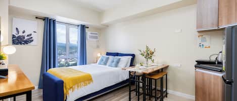 A bedroom with a bed, bedside table, and a small kitchen area with a refrigerator and a sink.